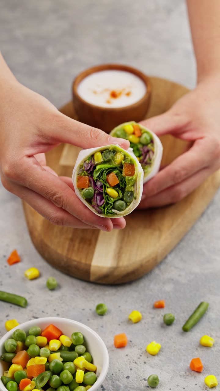 Manos partiendo un wrap de verduras sobre una tabla de madera